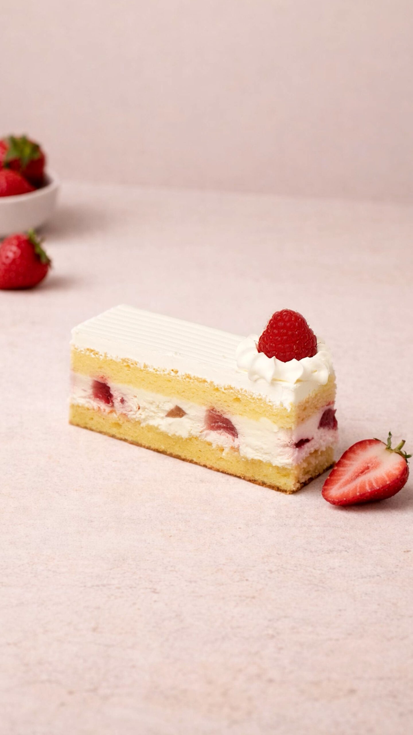 Strawberry slice. Rectangular pale cake slice with a smooth white top, visible red fruit pieces in the middle, and a red berry garnish.