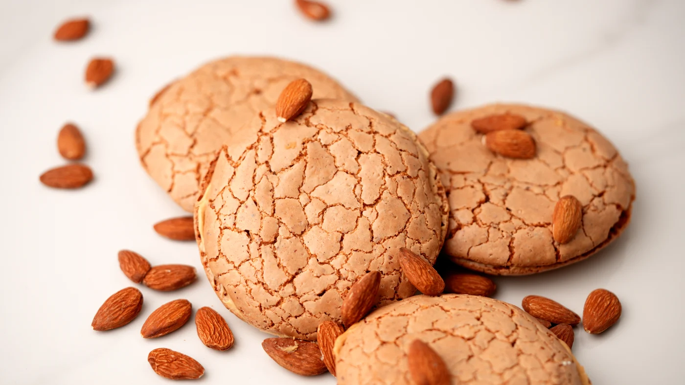 Almond slice. Golden round cookies with crackled surfaces and small brown oval pieces on top, scattered across a pale background.