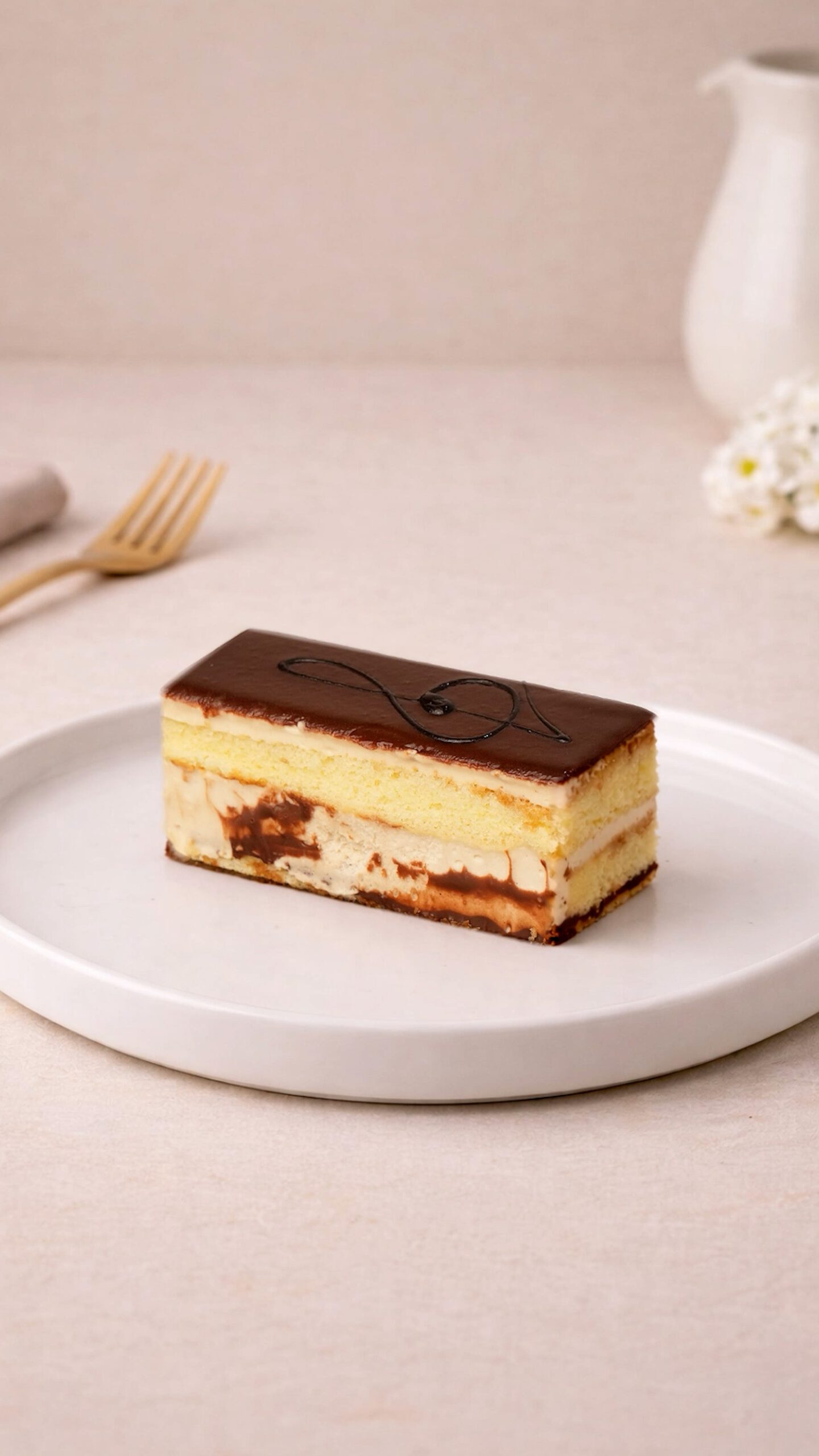 Opera slice. Rectangular layered cake slice with a dark glossy top, a fine curved decoration, and contrasting pale and brown layers.