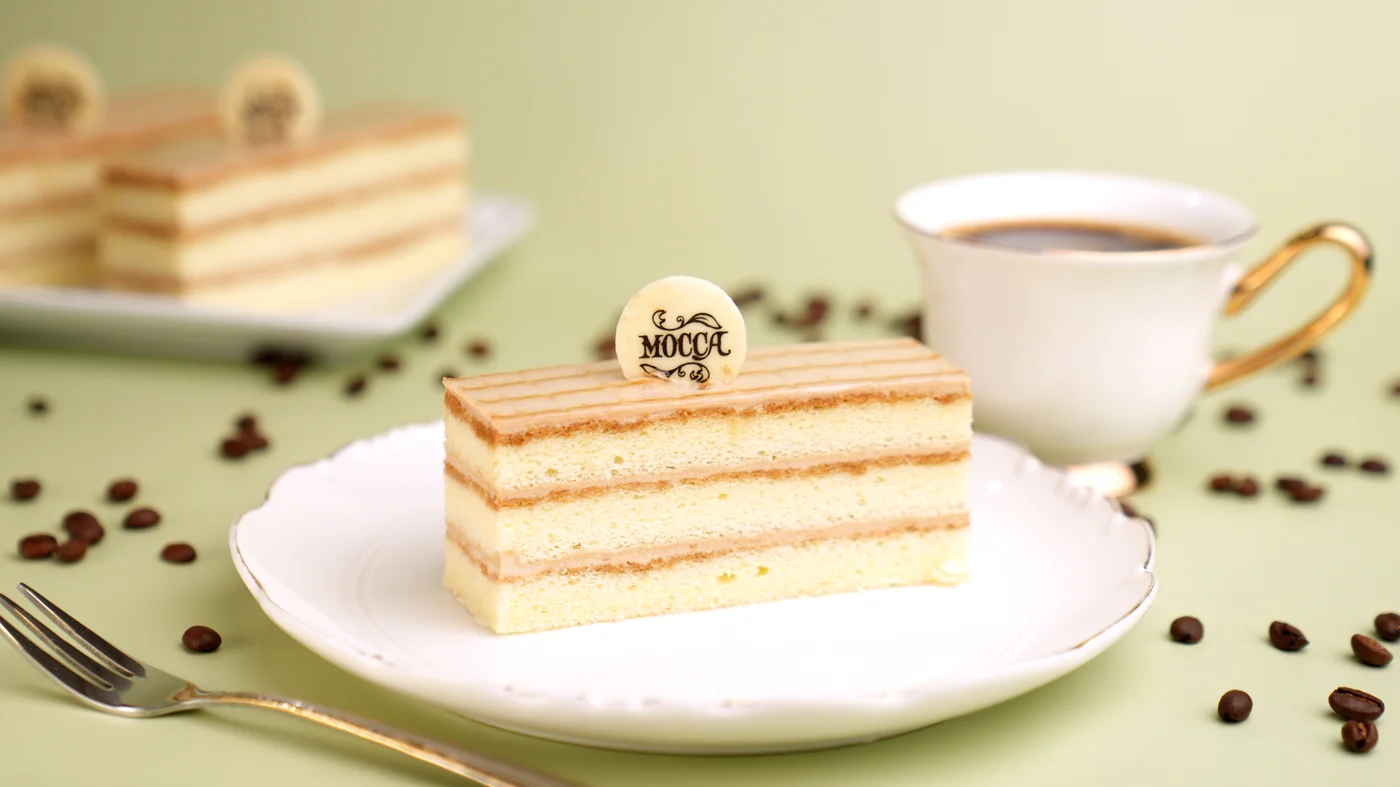Mocha slice. Rectangular pale cake slice with thin brown layers, fine parallel lines on top, and a small round label.