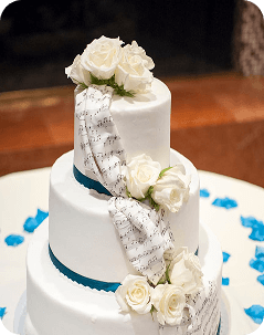 Three-tier white cake with dark blue ribbon bands, white flowers and a silver patterned cascade.