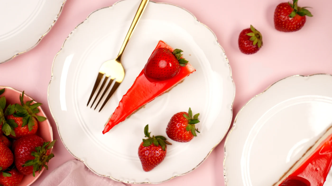Cheese cake slice. Triangular cake slice with a glossy bright red top and red berry garnish, photographed from above on a white plate.