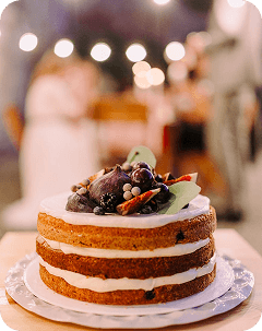Round cake with exposed brown layers, white filling and berries on top.