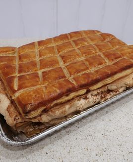 Baklava cake. Large rectangular golden pastry with a scored grid on top and thick pale and brown layers visible at the edge.