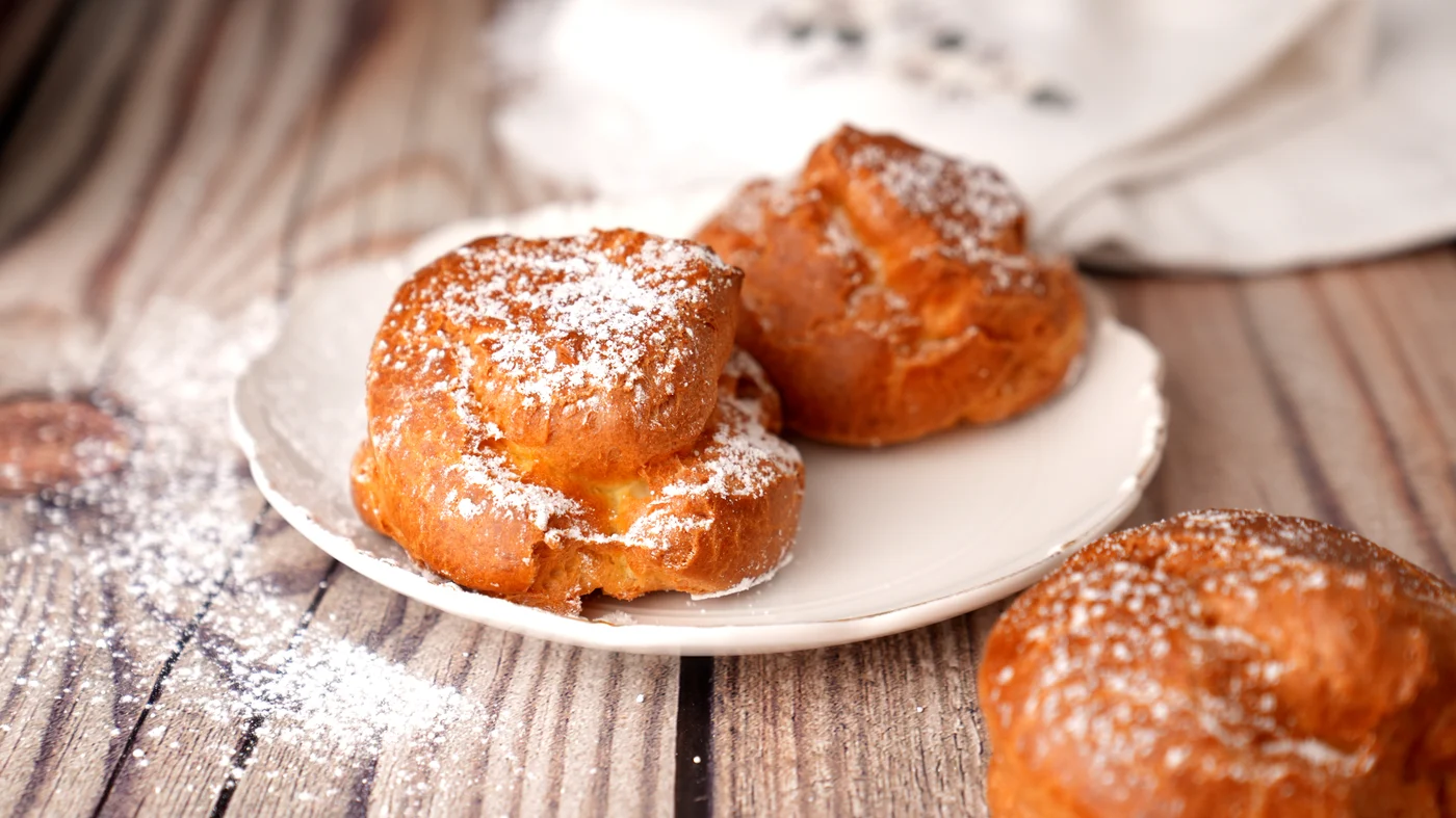 Cream puff. Three round golden pastries split around pale filling and dusted with white powder on a white plate.