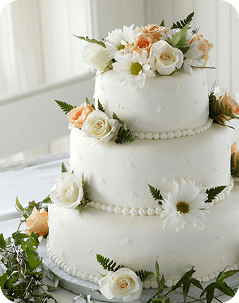 Three-tier white cake decorated with white flowers and green leaves.
