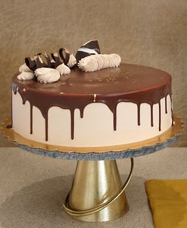 Chocolate cake. Round pale tan cake with a smooth dark top, long dark drips, pale piped swirls, and dark triangular decorations.